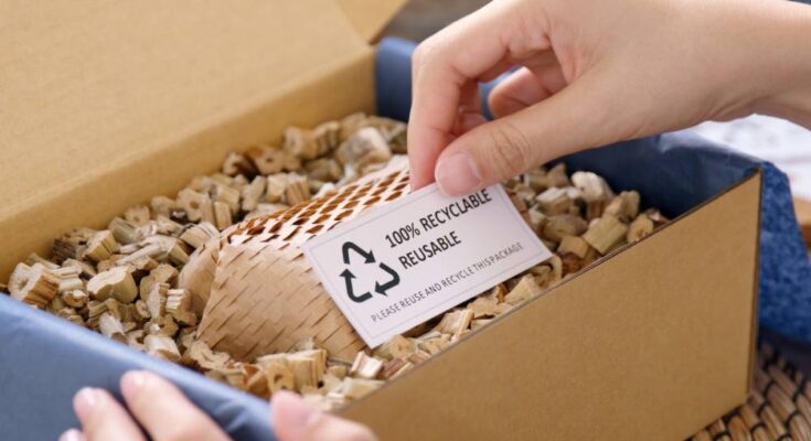 Two hands opening a cardboard box. One hand holds up a card in the box that reads “100% RECYCLABLE REUSABLE.”