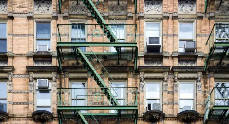 An old residential building with multiple stories and fire escapes. The building is brick and the escapes are green.