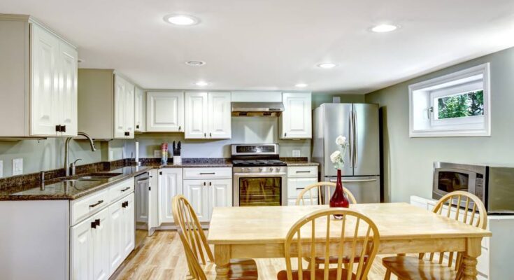 A newly renovated basement with counters, drawers, cabinets, a kitchen table set, refrigerator, oven, and microwave.