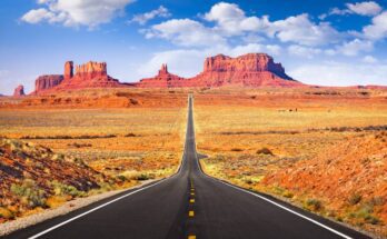 A paved road going through the center of Monument Valley toward distant mesas and buttes with a rocky landscape on each side.