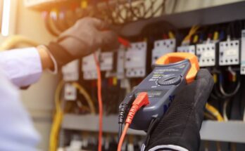 An engineer using a digital multimeter checks the electrical current voltage at a circuit breaker board.