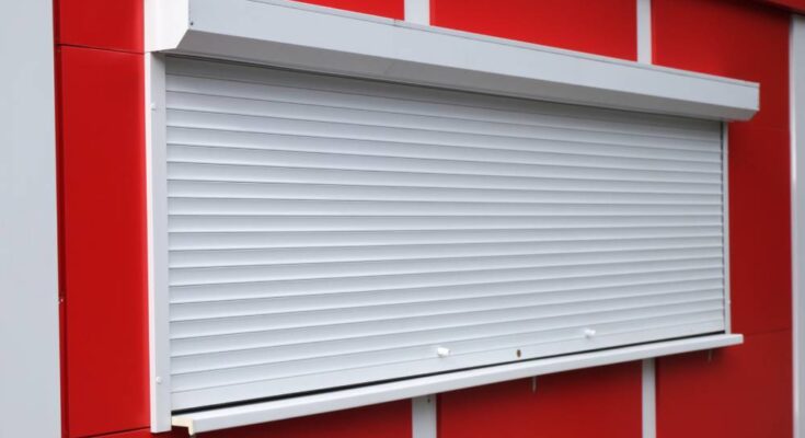 A white rolling security shutter closed over a transaction window. The surrounding wall consists of bright red panels.