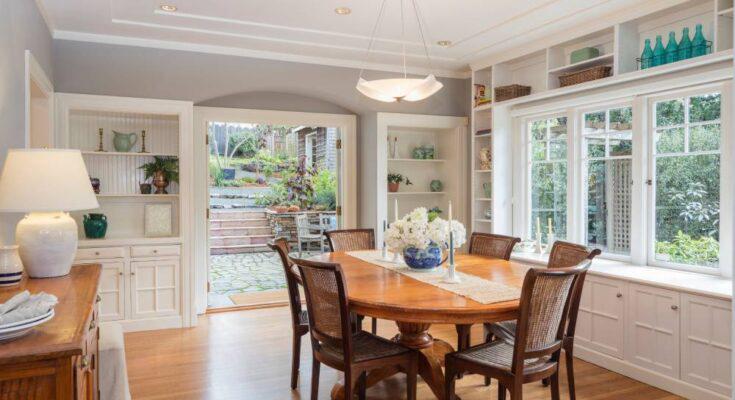 A traditional family dining room with shelving and hidden cabinets around the room. There's a bay window with a ledge.