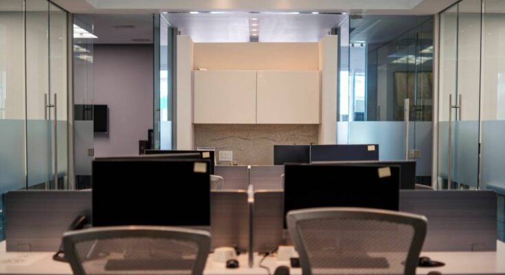 A shared office space with different desk spaces, all with computer monitors. There's a partition between each space.