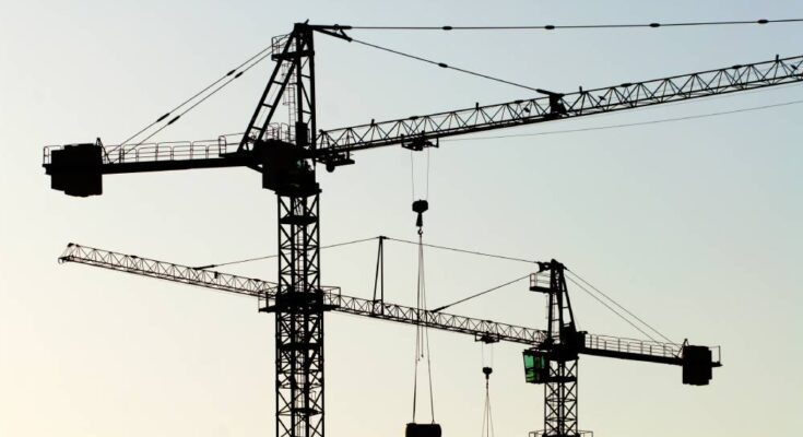 Two large construction cranes hoisted into the air with two pulley systems carrying material. The cranes are black.