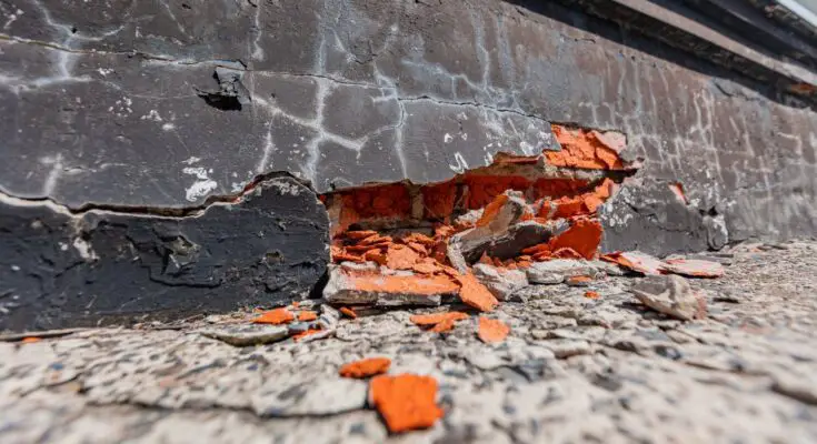 A cracked and crumbling foundation. The wall is mostly black, but the pieces coming out of it are bright orange.