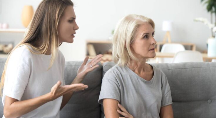 An annoyed young woman and her older mother on a couch. The daughter is gesturing toward her mother, who is turned away.