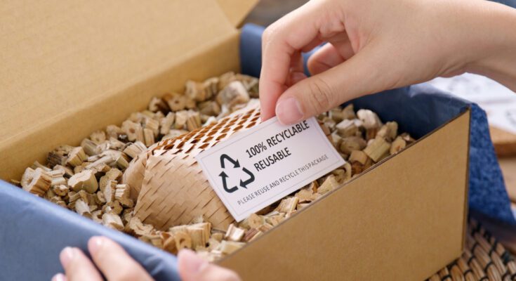 A person is opening a box with biodegradable packing filler and a white paper that says "100% recyclable reusable" inside.