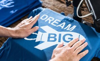 A pair of hands framing a blue graphic T-shirt that reads "dream big" with a white graphic of a rocket ship.