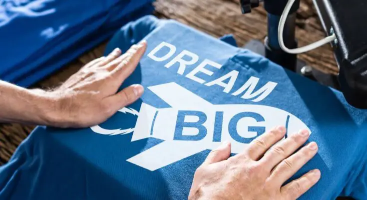 A pair of hands framing a blue graphic T-shirt that reads "dream big" with a white graphic of a rocket ship.