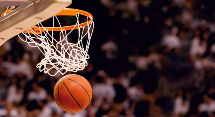 A basketball exiting a swooshing net after scoring a point. In the background is a blurry stand full of spectators.