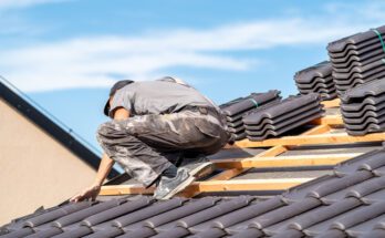 A professional roof installer works on a home's roof. Ceramic tile materials are organized in piles close to him.