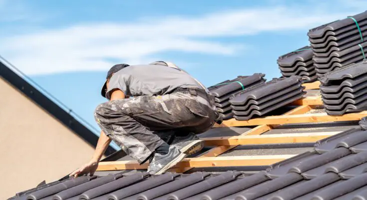 A professional roof installer works on a home's roof. Ceramic tile materials are organized in piles close to him.