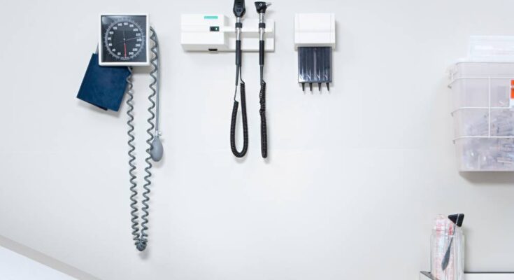 A blood pressure monitor and other equipment is mounted on a white wall in a clean doctor's office.