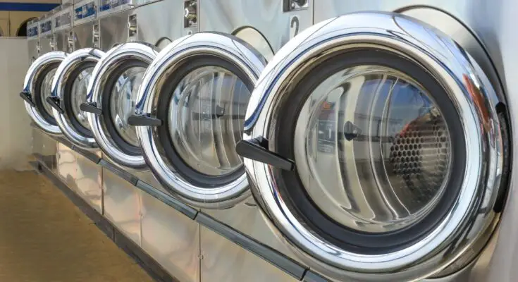 A row of five washing machines, all with their front doors open at the same angle. Each machine is shiny and clean.