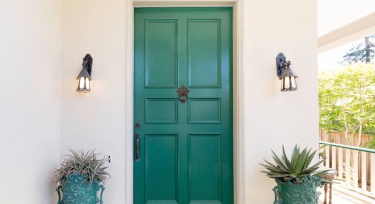 A white home with a shaded front entryway. The front door is teal and there's two matching teal planters on either side.