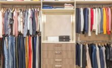 A wooden closet system with clothing on both sides separated by shelves in the center. Purses are on the top shelf.